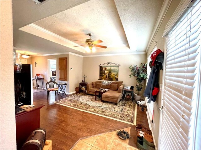 living room with a textured ceiling, ornamental molding, a raised ceiling, hardwood / wood-style flooring, and ceiling fan