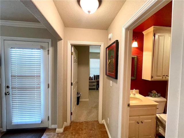 corridor with ornamental molding, sink, tile patterned floors, and a textured ceiling