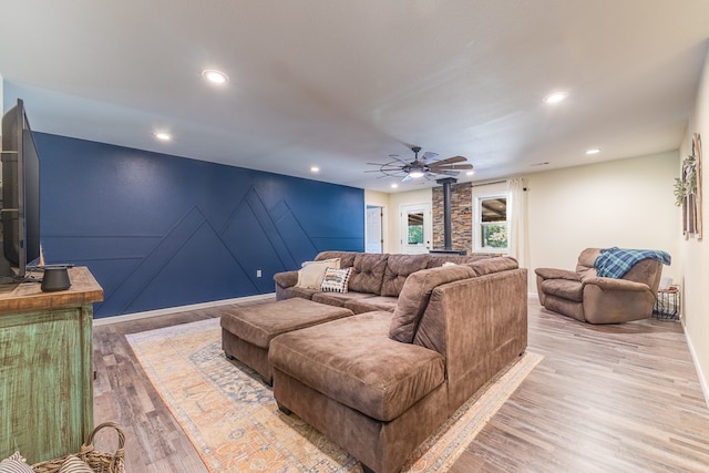 living room featuring ceiling fan, light wood-type flooring, and a wood stove