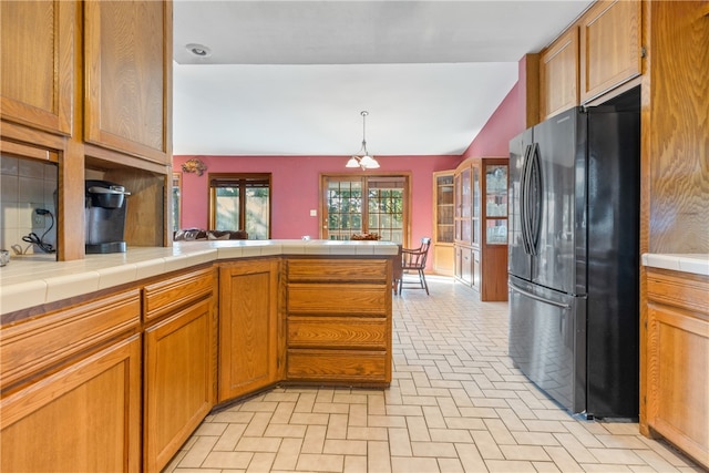 kitchen featuring lofted ceiling, hanging light fixtures, kitchen peninsula, tile countertops, and black refrigerator