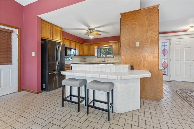 kitchen featuring ceiling fan, tasteful backsplash, a kitchen breakfast bar, stainless steel appliances, and tile counters