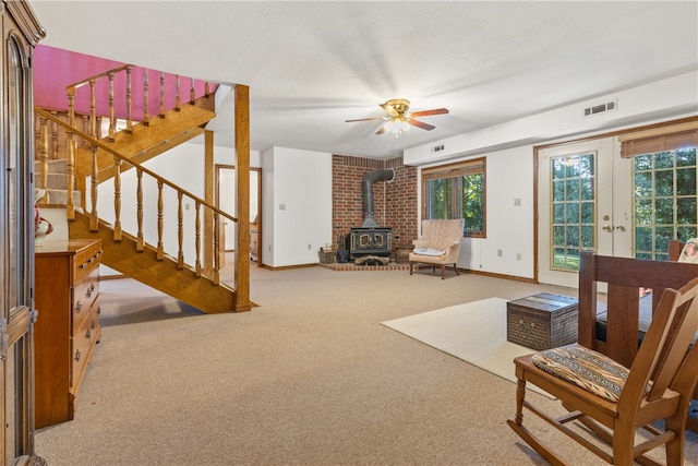 carpeted living room with a wood stove and ceiling fan