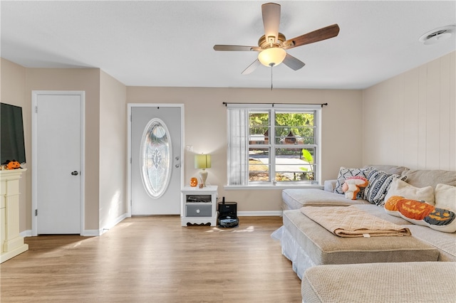 living room featuring ceiling fan, light wood-type flooring, and wood walls