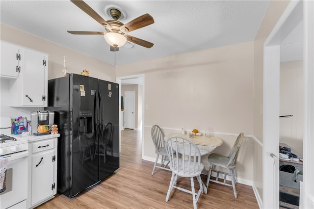 kitchen with light hardwood / wood-style floors, white gas range oven, white cabinets, decorative backsplash, and black refrigerator with ice dispenser