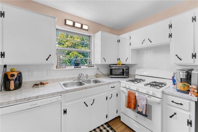 kitchen featuring sink, white appliances, backsplash, white cabinetry, and hardwood / wood-style flooring