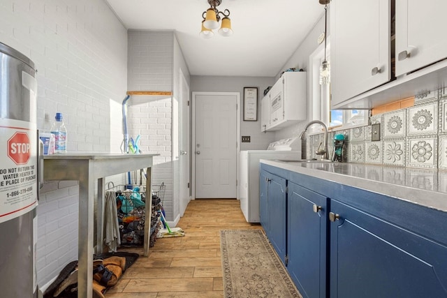 kitchen with blue cabinets, washing machine and dryer, brick wall, white cabinets, and light wood-type flooring