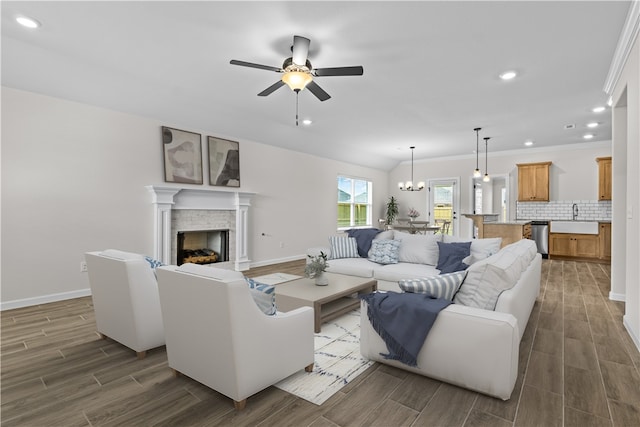 living room with ceiling fan with notable chandelier, a fireplace, dark wood-type flooring, and sink