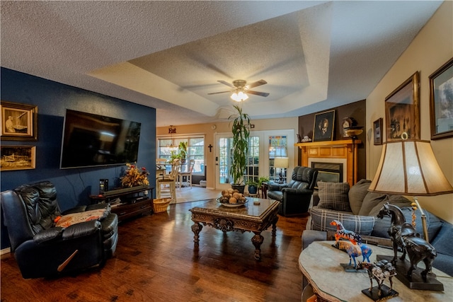 living room with french doors, dark hardwood / wood-style flooring, a textured ceiling, a raised ceiling, and ceiling fan