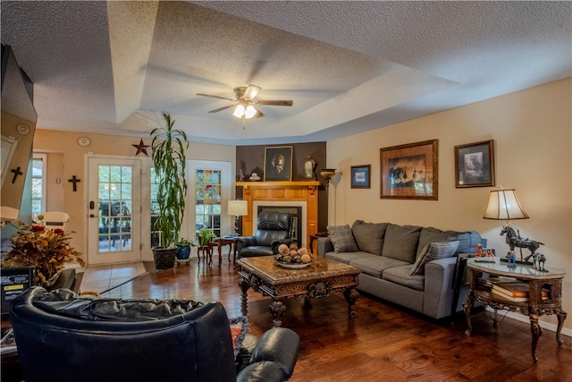 living room featuring a textured ceiling, ceiling fan, dark wood-type flooring, and a tray ceiling