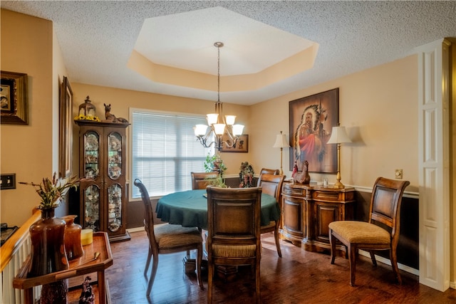 dining room featuring a textured ceiling, dark hardwood / wood-style floors, an inviting chandelier, and a tray ceiling