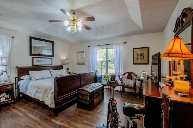 bedroom with ceiling fan, dark hardwood / wood-style flooring, a textured ceiling, and a tray ceiling