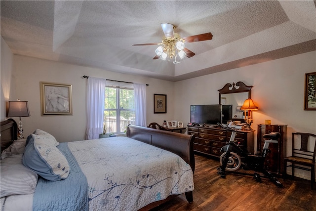 bedroom with a textured ceiling, dark hardwood / wood-style flooring, a raised ceiling, and ceiling fan