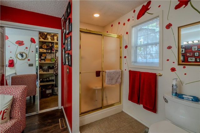 bathroom featuring toilet, an enclosed shower, a textured ceiling, and hardwood / wood-style flooring