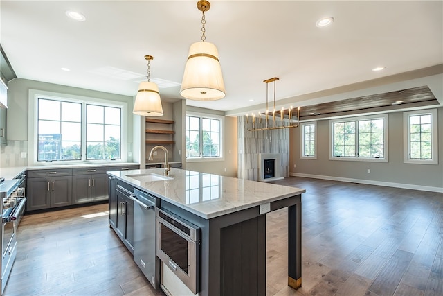 kitchen with an island with sink, decorative light fixtures, sink, and a healthy amount of sunlight