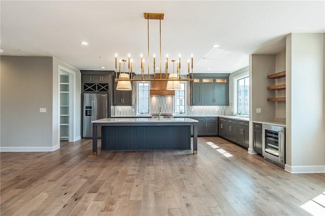 kitchen with pendant lighting, wine cooler, a kitchen island with sink, stainless steel fridge with ice dispenser, and light wood-type flooring