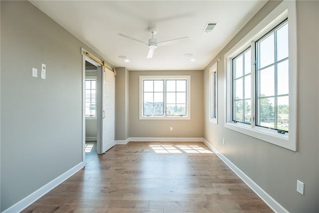 unfurnished room featuring a barn door, light hardwood / wood-style floors, and ceiling fan