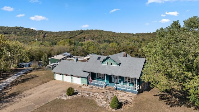 view of front of property featuring concrete driveway, a porch, a forest view, and an attached garage
