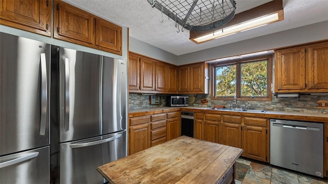 kitchen with appliances with stainless steel finishes, brown cabinetry, decorative backsplash, stone finish flooring, and a sink