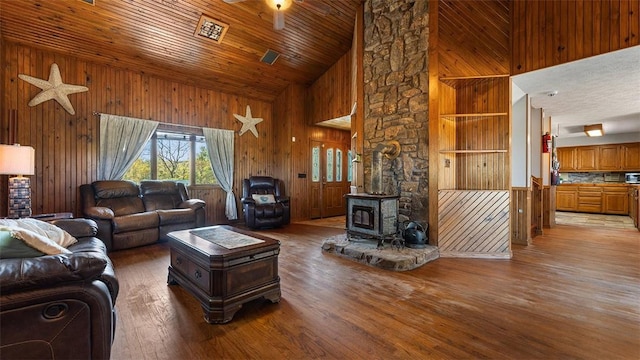 living area with light wood-type flooring, wood walls, ceiling fan, and a wood stove