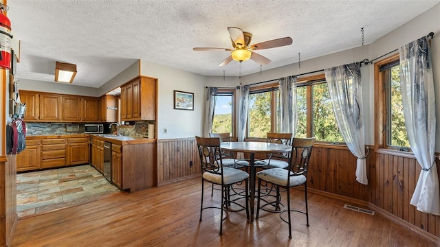 dining room with wood walls, wainscoting, light wood-type flooring, and a ceiling fan