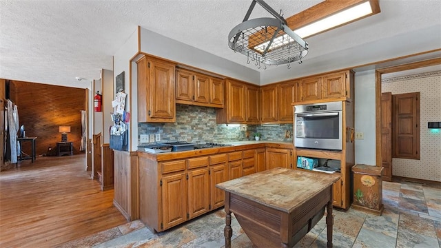 kitchen with oven, light countertops, stone finish floor, a textured ceiling, and wallpapered walls