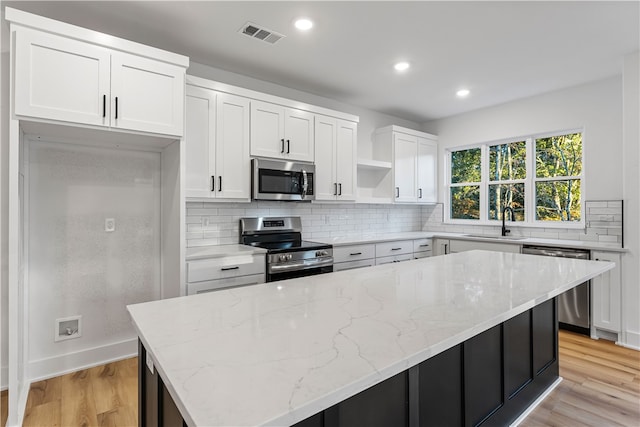 kitchen with a kitchen island, stainless steel appliances, light stone countertops, light wood-type flooring, and white cabinets