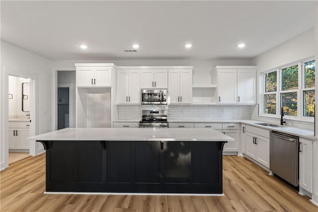 kitchen with open shelves, light wood-style floors, a center island, a sink, and appliances with stainless steel finishes