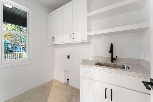 laundry area featuring cabinet space, a sink, electric dryer hookup, baseboards, and light tile patterned floors