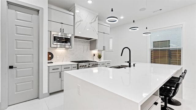 kitchen with sink, an island with sink, a kitchen bar, stainless steel appliances, and backsplash