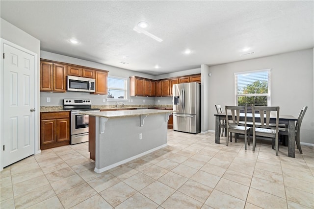 kitchen with light stone counters, light tile patterned floors, appliances with stainless steel finishes, a center island, and a breakfast bar area