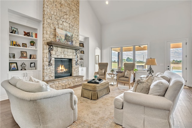 living room featuring light hardwood / wood-style floors, a stone fireplace, built in features, and high vaulted ceiling