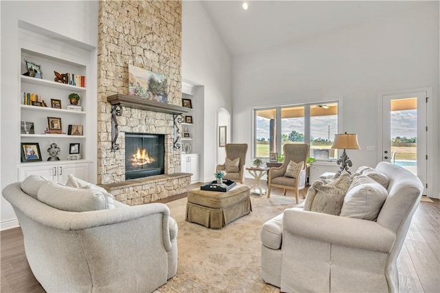 living room with high vaulted ceiling, a wealth of natural light, a stone fireplace, and wood finished floors