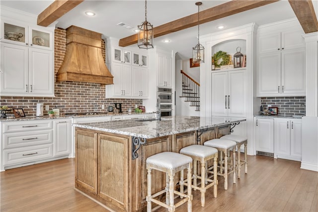 kitchen with beamed ceiling, a center island with sink, white cabinetry, and light stone counters