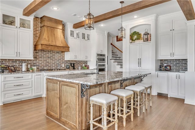 kitchen with tasteful backsplash, light wood-style floors, custom range hood, and beam ceiling