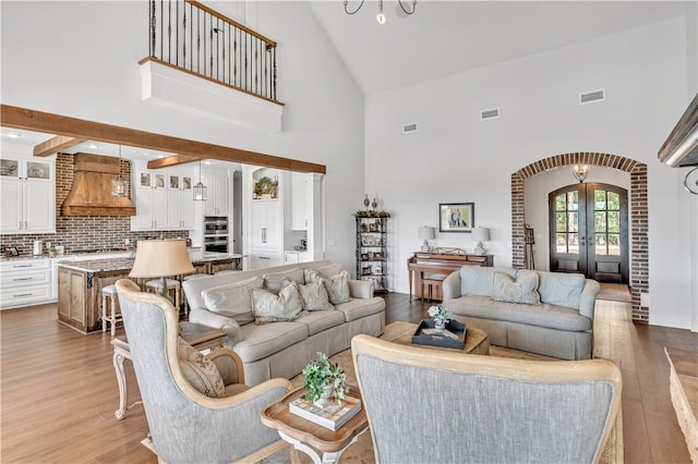 living room with french doors, a towering ceiling, and light hardwood / wood-style flooring