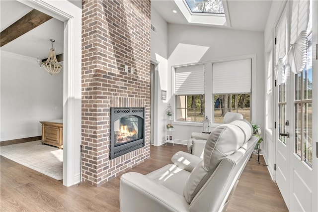 living room with beamed ceiling, a skylight, hardwood / wood-style flooring, and a brick fireplace