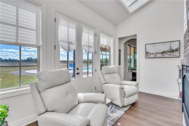 living area featuring vaulted ceiling with skylight, wood finished floors, and baseboards