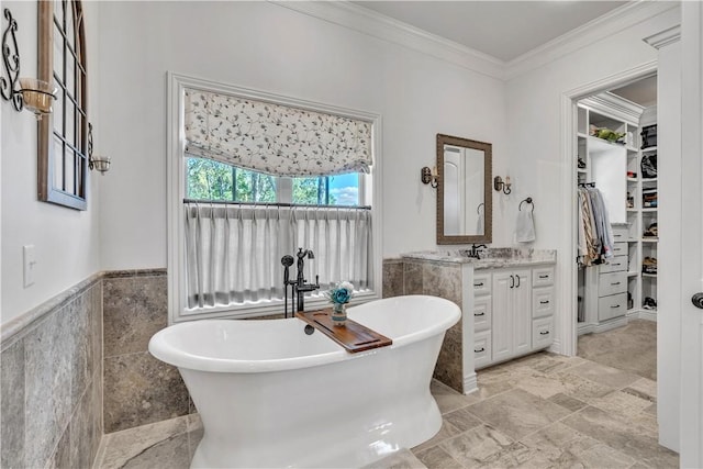 bathroom with a soaking tub, vanity, ornamental molding, a walk in closet, and tile walls