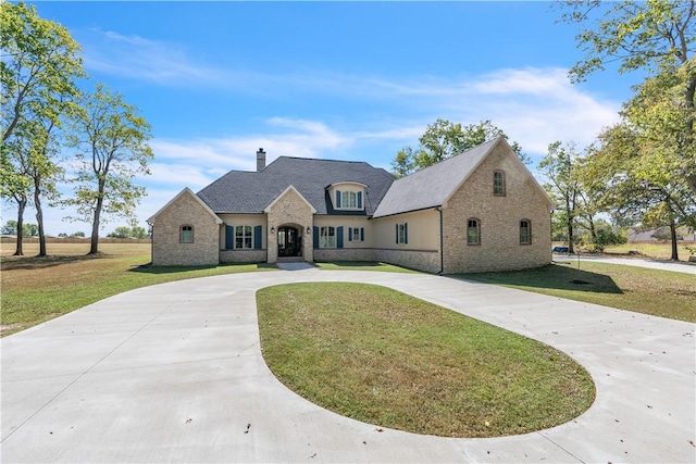 view of front facade featuring curved driveway, stone siding, a front lawn, and a chimney