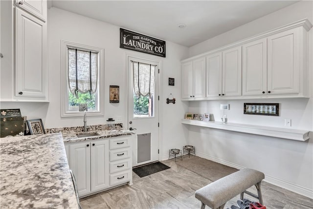 kitchen featuring a sink, baseboards, white cabinetry, and light stone countertops