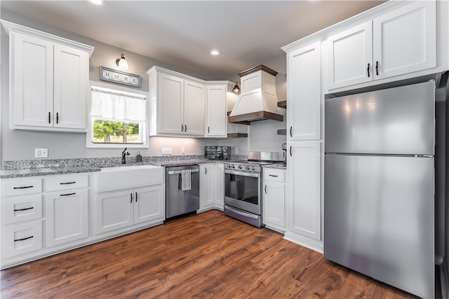 kitchen with appliances with stainless steel finishes, white cabinets, light stone countertops, premium range hood, and dark hardwood / wood-style floors