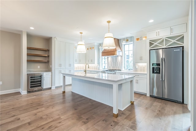 kitchen with pendant lighting, wine cooler, white cabinets, stainless steel appliances, and premium range hood