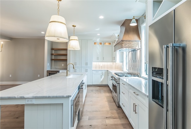 kitchen with white cabinets, premium range hood, sink, premium appliances, and a large island with sink