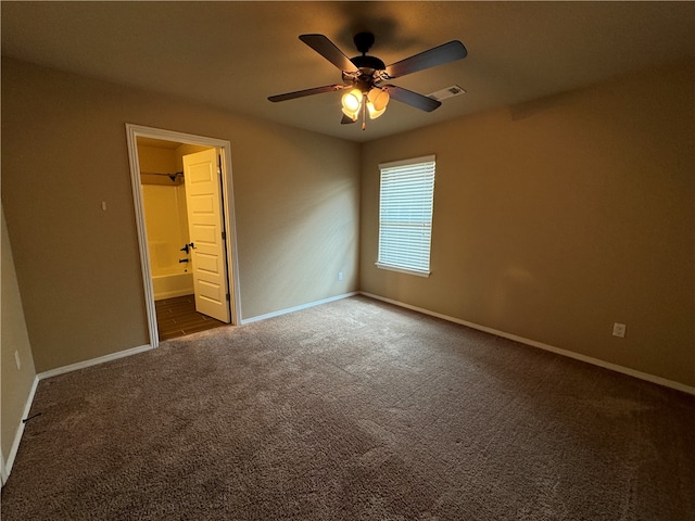 unfurnished bedroom featuring ceiling fan, ensuite bathroom, and dark carpet