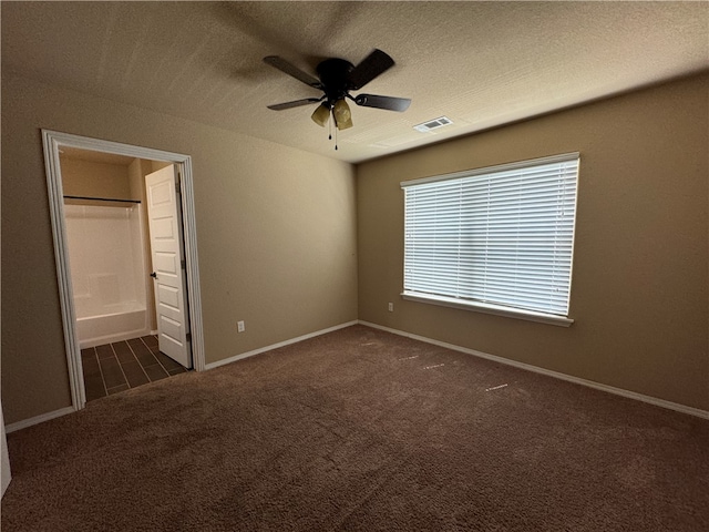 unfurnished bedroom with a textured ceiling, dark colored carpet, ceiling fan, and ensuite bathroom