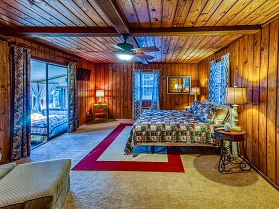 carpeted bedroom with beam ceiling, ceiling fan, wood ceiling, and wood walls