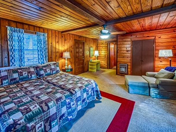 bedroom with wooden ceiling, wooden walls, carpet flooring, ceiling fan, and beamed ceiling