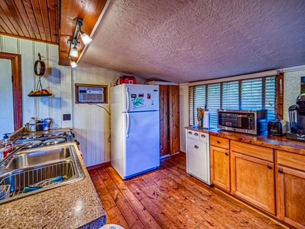 kitchen featuring white appliances, vaulted ceiling, wooden walls, dark wood-type flooring, and sink