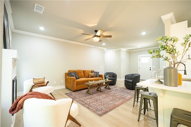 living room featuring ornamental molding, light wood-type flooring, and ceiling fan