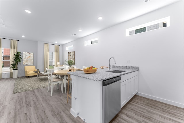 kitchen with sink, kitchen peninsula, stainless steel dishwasher, white cabinetry, and light hardwood / wood-style floors